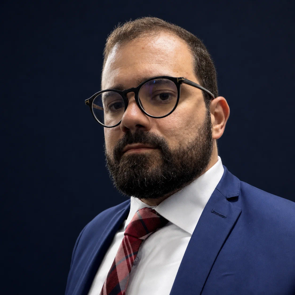 Retrato profissional de Leonardo Athayde, de terno azul e gravata, sobre fundo escuro